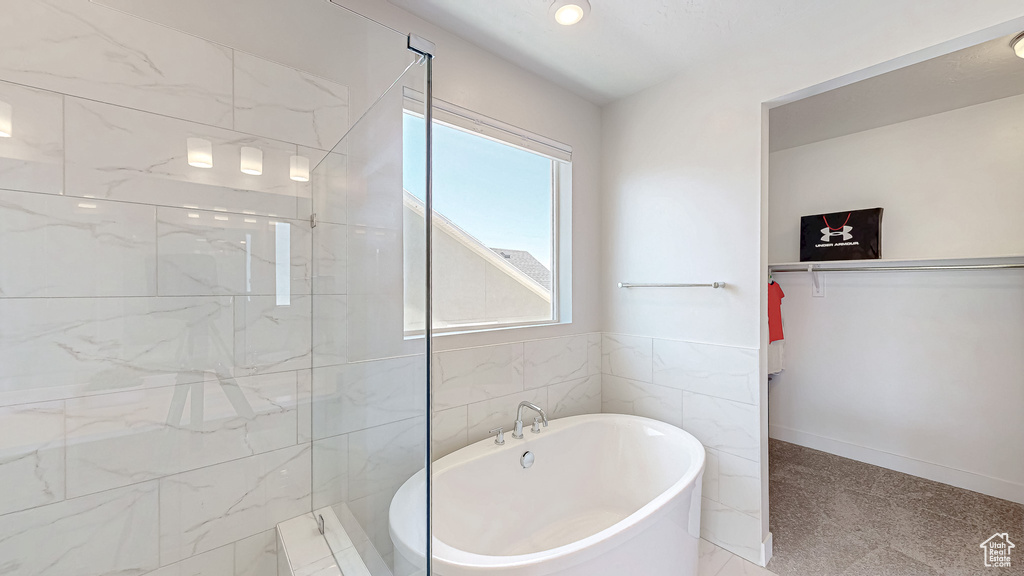 Full bathroom with a freestanding tub, tiled shower, a walk in closet, and tile walls