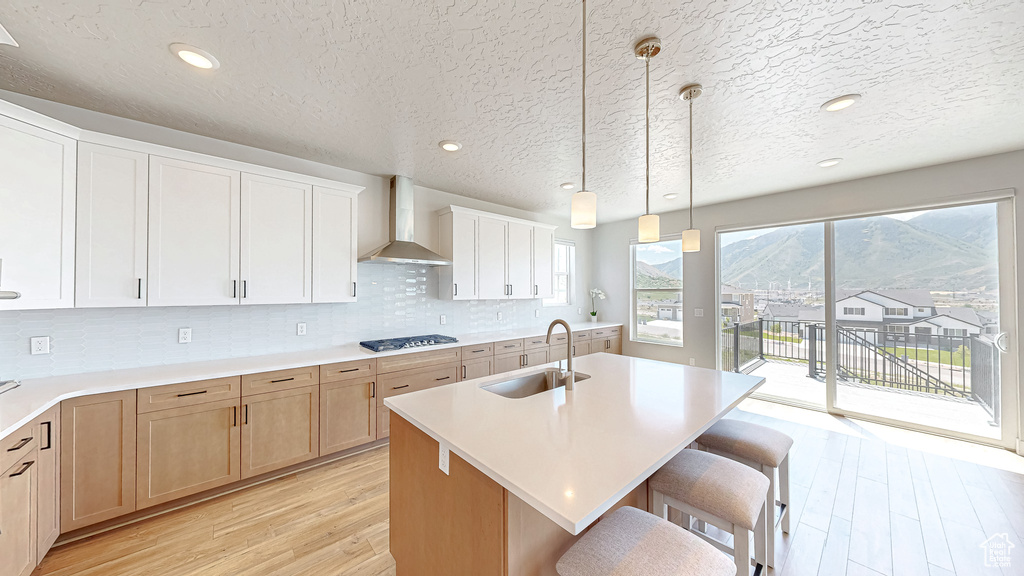 Kitchen featuring wall chimney range hood, a sink, light wood-style floors, gas cooktop, and light countertops