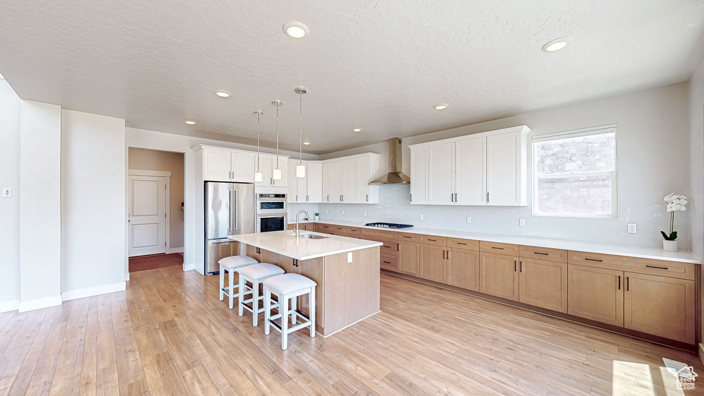 Kitchen with stainless steel appliances, a sink, a kitchen breakfast bar, wall chimney range hood, and light countertops