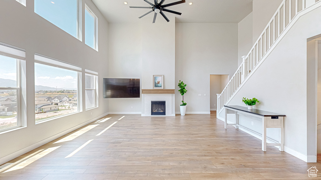 Unfurnished living room with a towering ceiling, healthy amount of natural light, ceiling fan, and light wood-style flooring