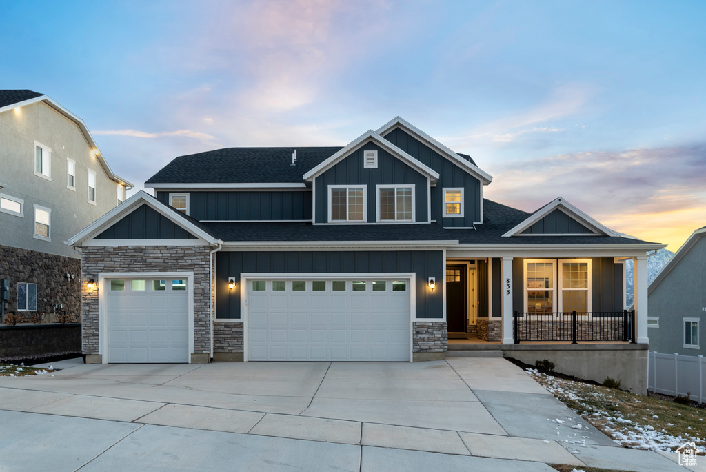 View of front facade featuring board and batten siding, a porch, stone siding, and driveway