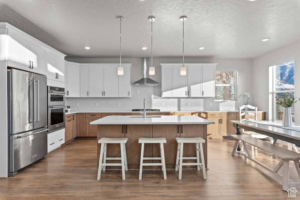 Kitchen featuring appliances with stainless steel finishes, wall chimney exhaust hood, dark wood-style floors, light countertops, and recessed lighting