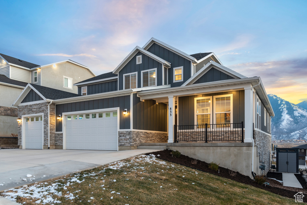 View of front of house with board and batten siding, a porch, driveway, an attached garage, and stone siding