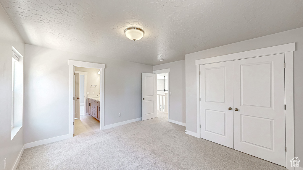 Unfurnished bedroom with light colored carpet, baseboards, a textured ceiling, a closet, and connected bathroom