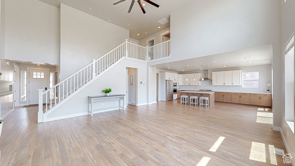 Living area featuring a high ceiling, a ceiling fan, stairway, light wood-style flooring, and baseboards