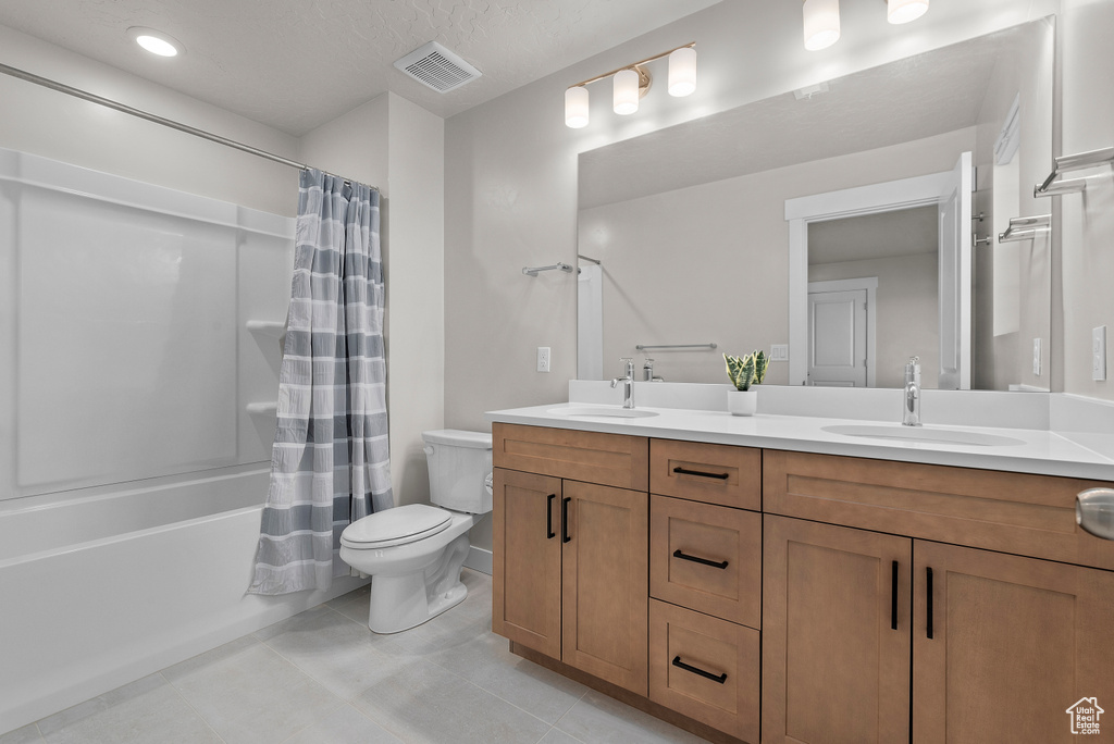 Full bathroom featuring double vanity, toilet, shower / bath combination with curtain, and tile patterned floors