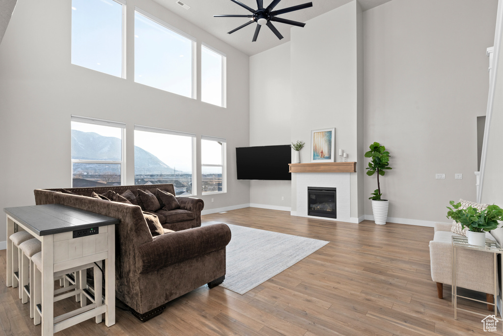 Living area with a towering ceiling, a glass covered fireplace, baseboards, and wood finished floors