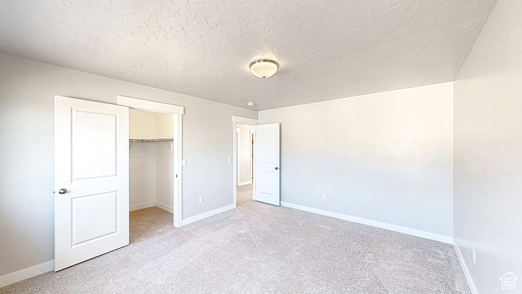 Unfurnished bedroom with baseboards, carpet flooring, a spacious closet, and a textured ceiling