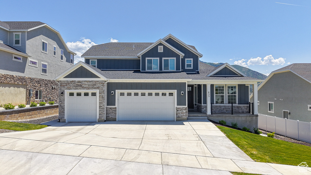 View of front of property featuring board and batten siding, stone siding, covered porch, concrete driveway, and a shingled roof