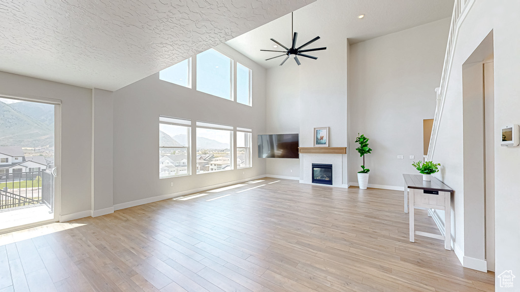 Unfurnished living room with a glass covered fireplace, light wood finished floors, baseboards, a textured ceiling, and a ceiling fan