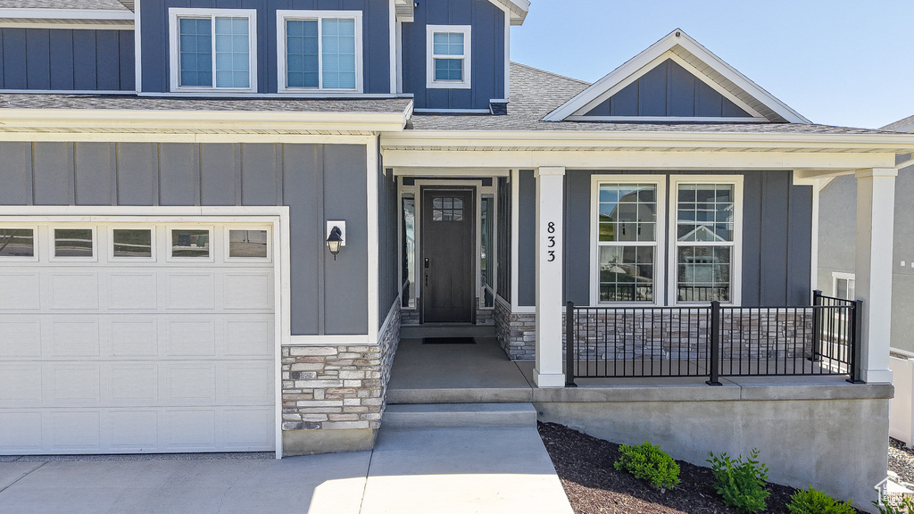 View of exterior entry featuring a porch, board and batten siding, roof with shingles, and stone siding