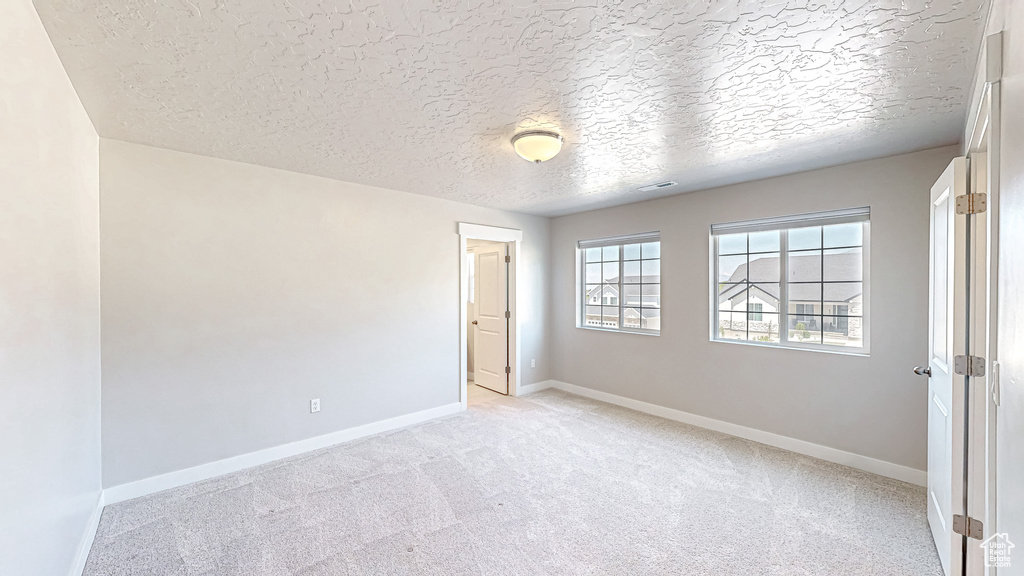 Empty room featuring a textured ceiling, light colored carpet, and baseboards