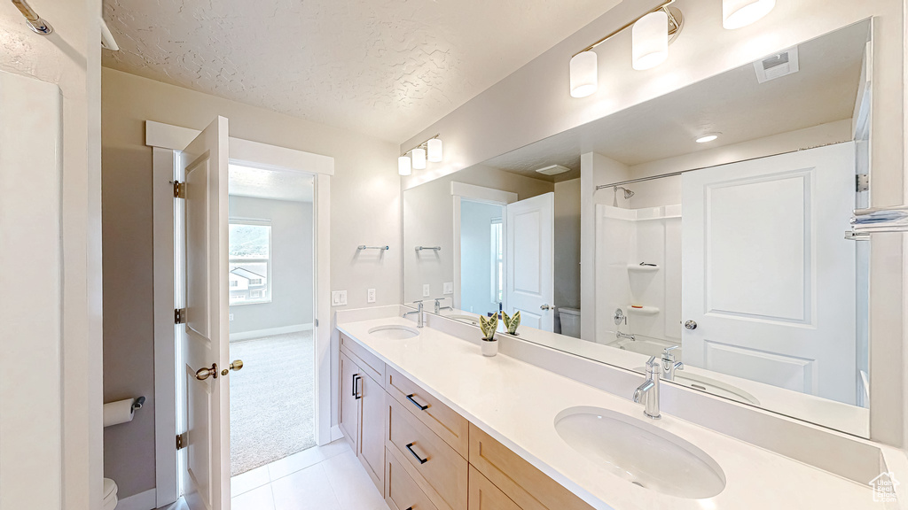 Bathroom featuring toilet, double vanity, tile patterned flooring, a textured ceiling, and baseboards
