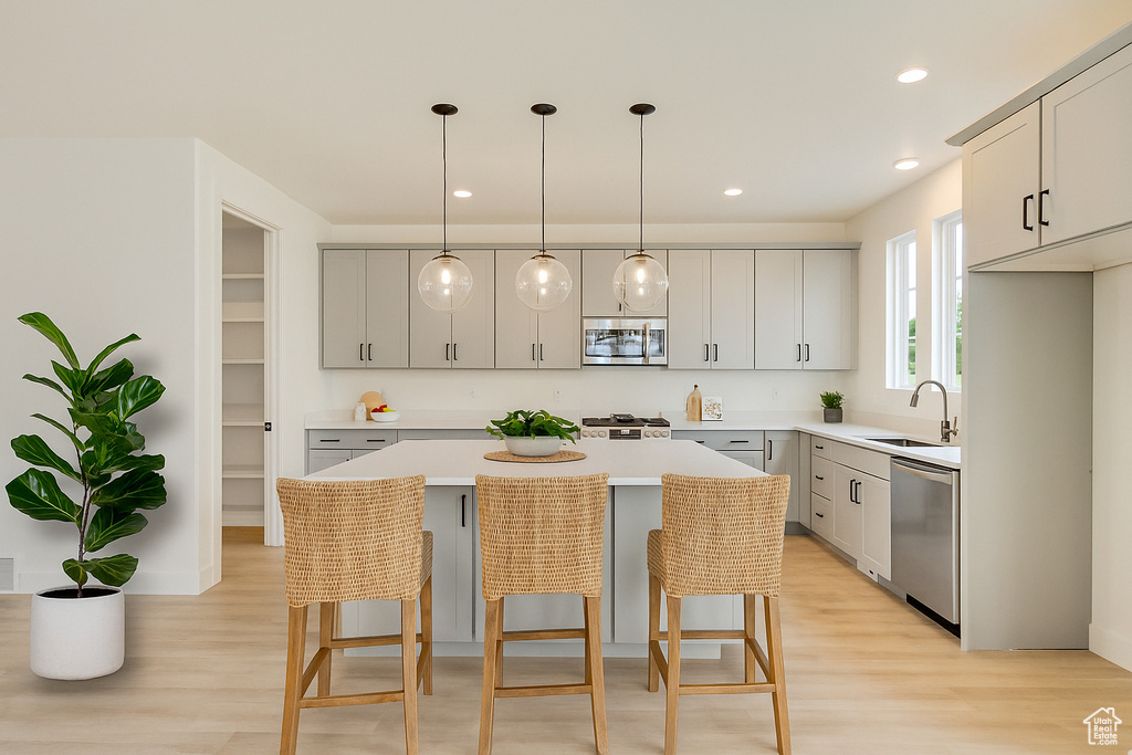 Kitchen with appliances with stainless steel finishes, light wood finished floors, gray cabinets, a kitchen bar, and recessed lighting