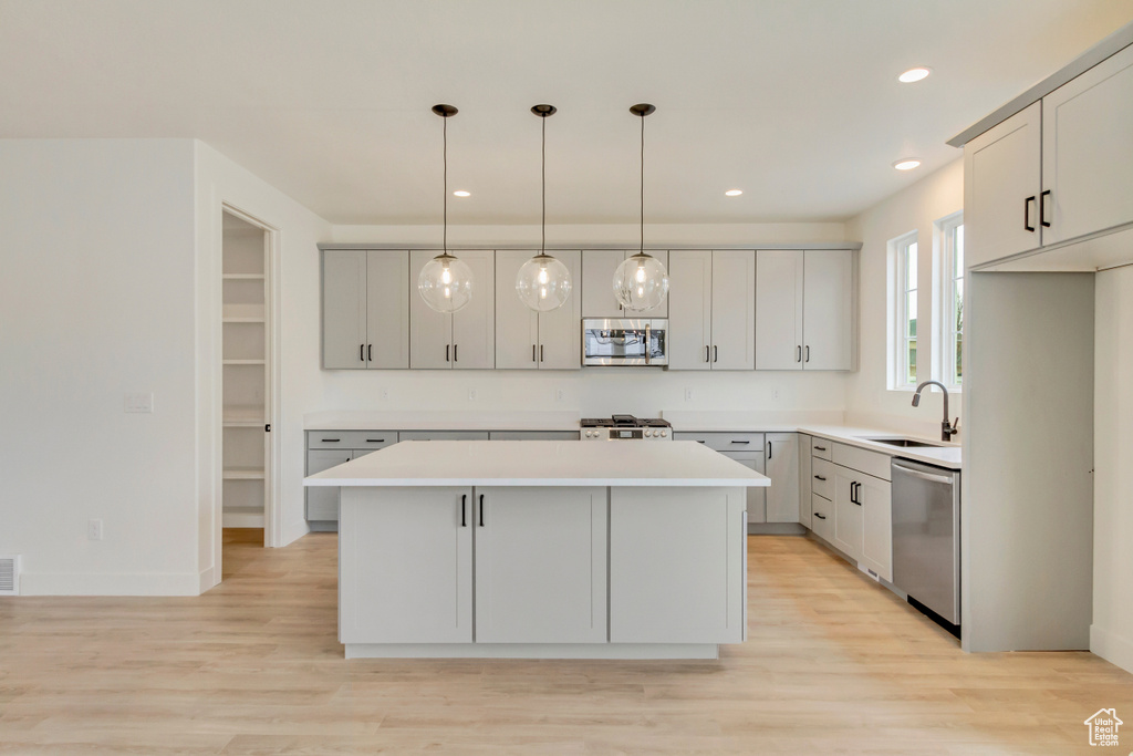 Kitchen featuring stainless steel appliances, a sink, a kitchen island, light countertops, and light wood finished floors