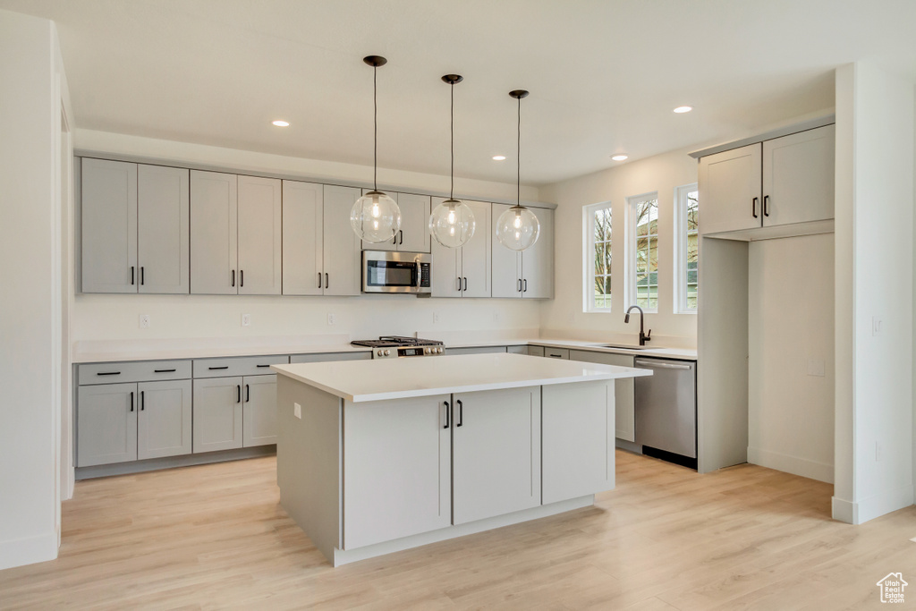 Kitchen with appliances with stainless steel finishes, a kitchen island, recessed lighting, light wood finished floors, and light countertops