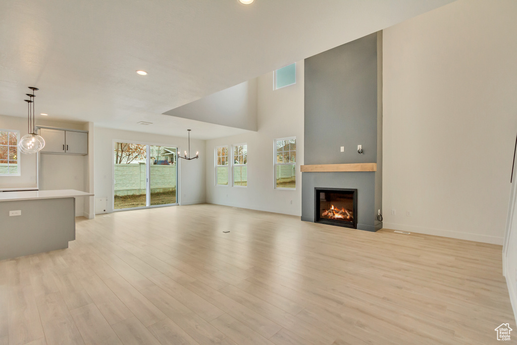 Unfurnished living room featuring a chandelier, a glass covered fireplace, light wood-style floors, and recessed lighting