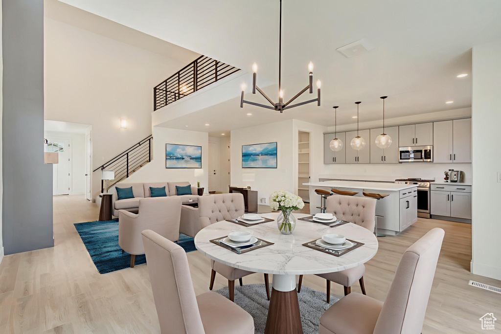 Dining room featuring light wood-style floors, recessed lighting, stairs, a chandelier, and a high ceiling