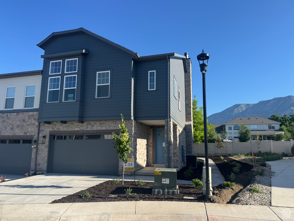 View of front of property with a mountain view, concrete driveway, cooling unit, an attached garage, and a chimney
