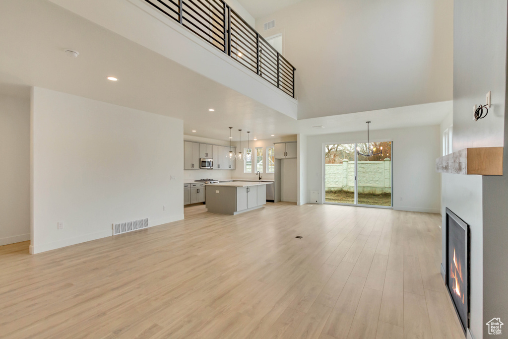 Unfurnished living room with a chandelier, a lit fireplace, a high ceiling, light wood-type flooring, and baseboards