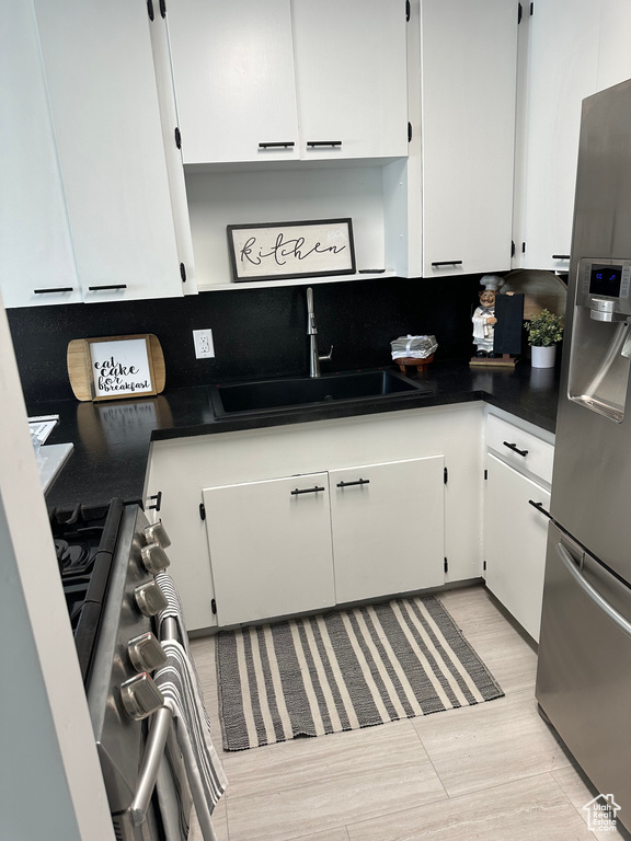 Kitchen with stainless steel fridge, a sink, white cabinets, and dark countertops