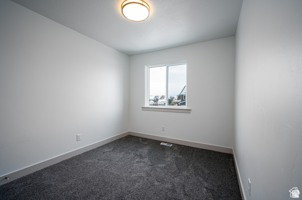 Spare room featuring dark colored carpet and baseboards
