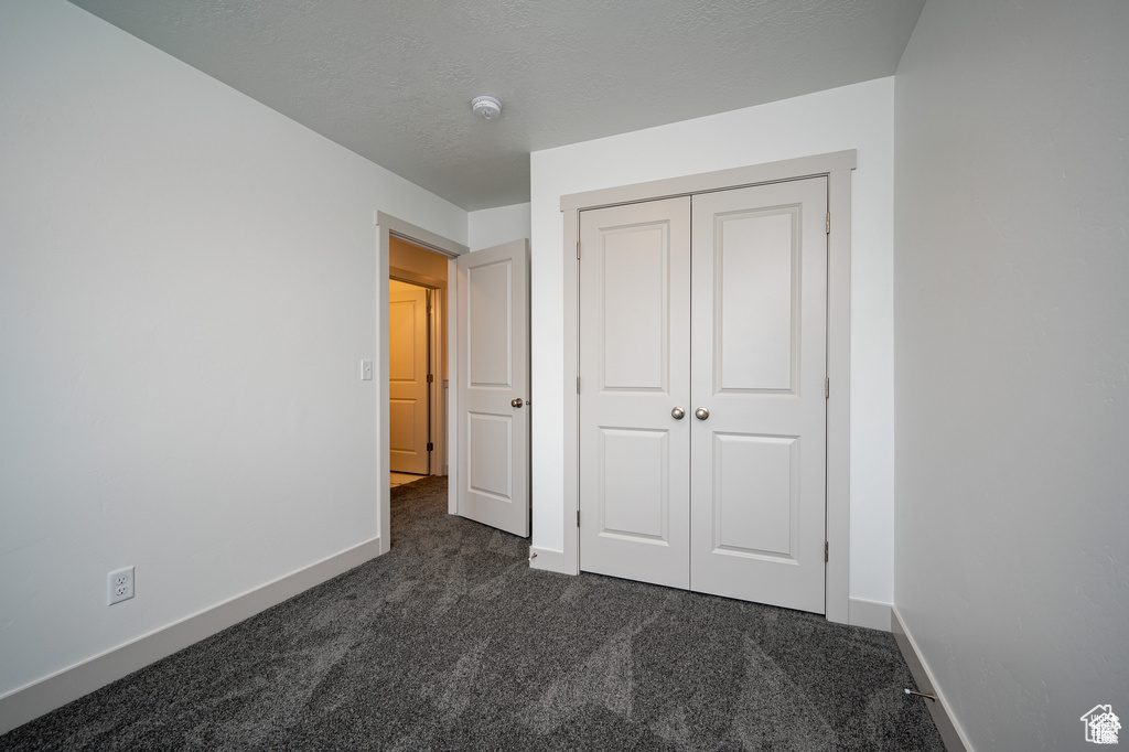 Unfurnished bedroom featuring dark carpet, baseboards, and a closet