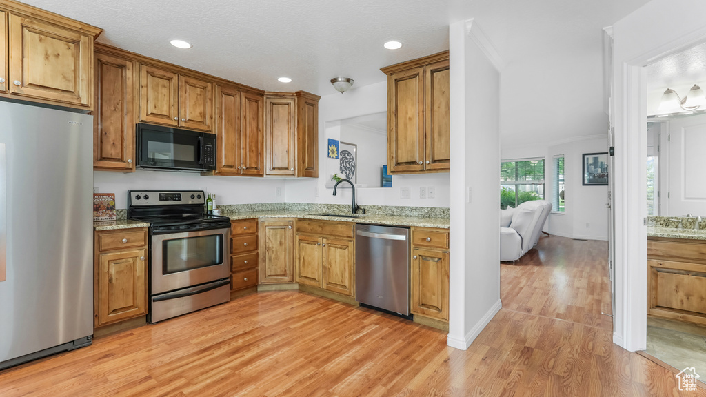 Kitchen featuring stainless steel appliances, a sink, brown cabinets, light wood-style floors, and recessed lighting
