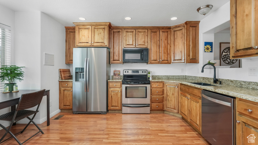 Kitchen featuring stainless steel appliances, a sink, light wood-style floors, brown cabinets, and light stone countertops