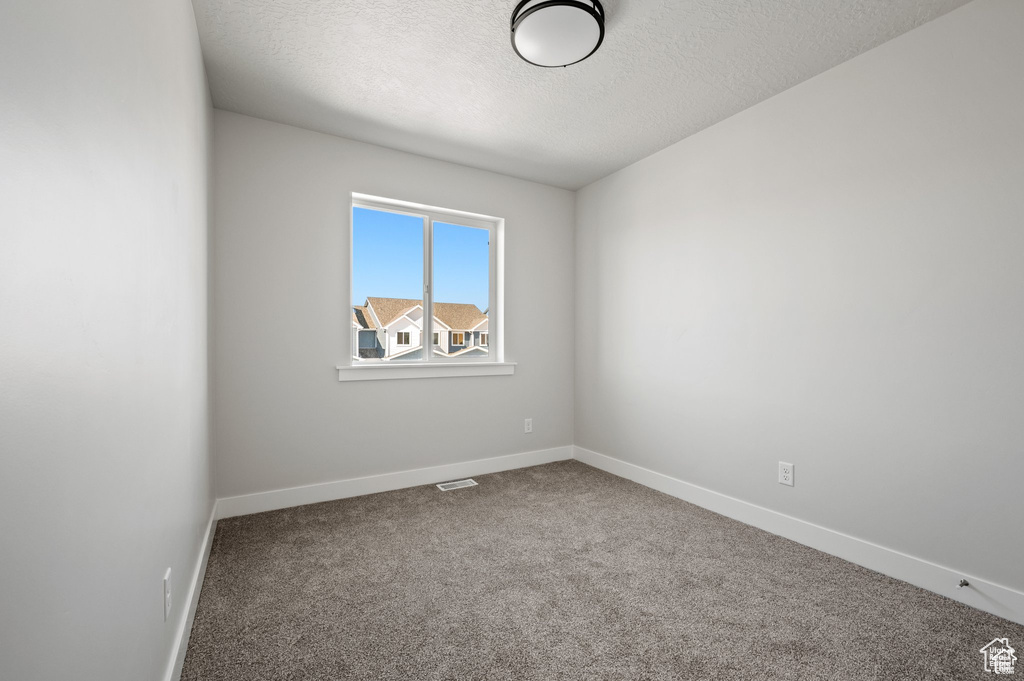 Carpeted empty room with a textured ceiling and baseboards