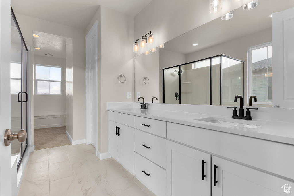 Full bathroom with double vanity, marble look tiles, a shower stall, and baseboards