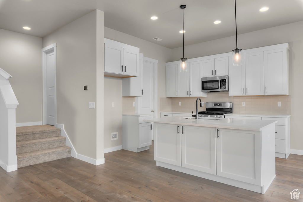 Kitchen with appliances with stainless steel finishes, wood finished floors, backsplash, light countertops, and baseboards