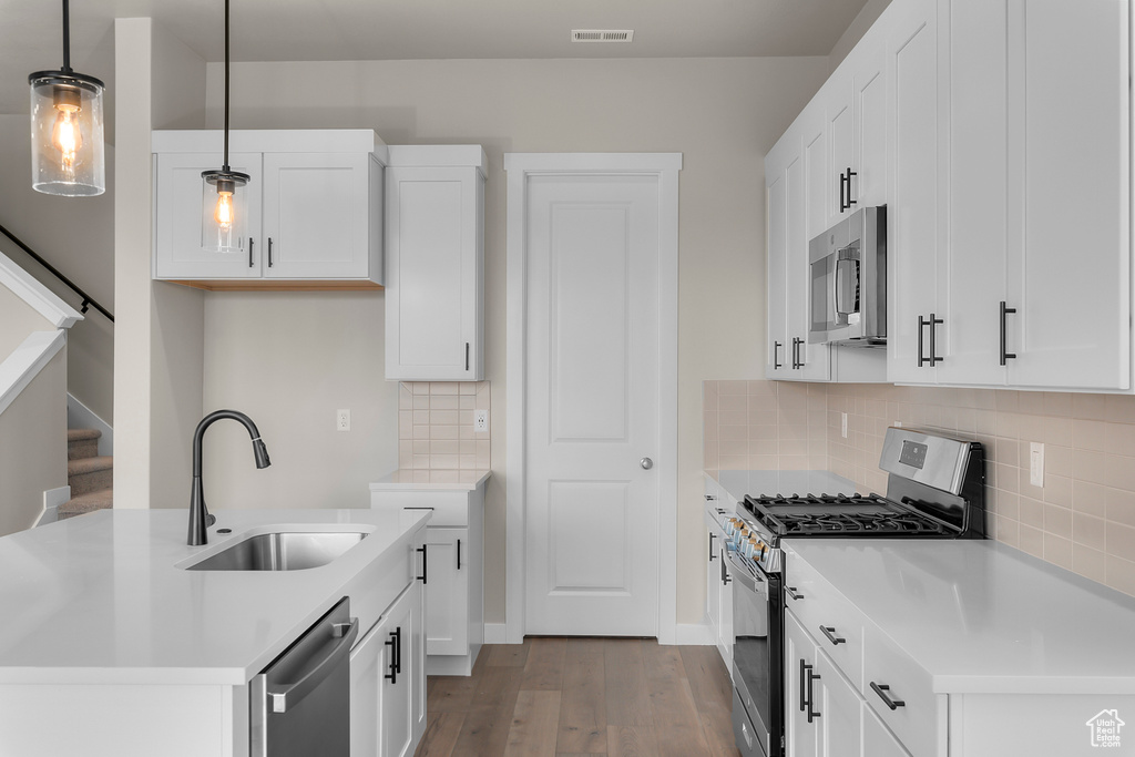 Kitchen with appliances with stainless steel finishes, a sink, wood finished floors, tasteful backsplash, and pendant lighting