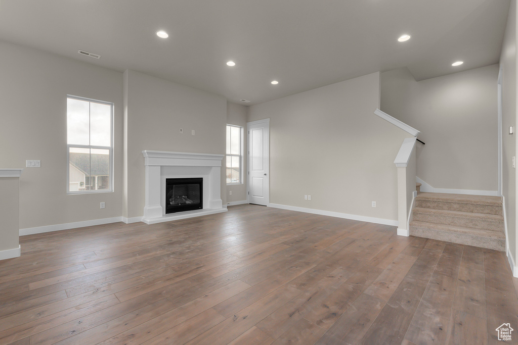 Unfurnished living room featuring a glass covered fireplace, hardwood / wood-style flooring, stairway, recessed lighting, and baseboards