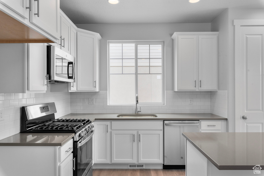 Kitchen featuring stainless steel appliances, a sink, white cabinets, recessed lighting, and decorative backsplash
