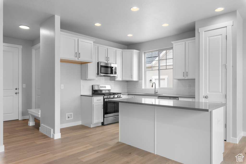 Kitchen featuring stainless steel appliances, a sink, white cabinetry, decorative backsplash, and recessed lighting