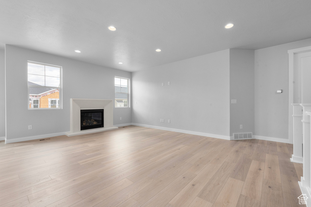 Unfurnished living room with a glass covered fireplace, recessed lighting, light wood-type flooring, and baseboards