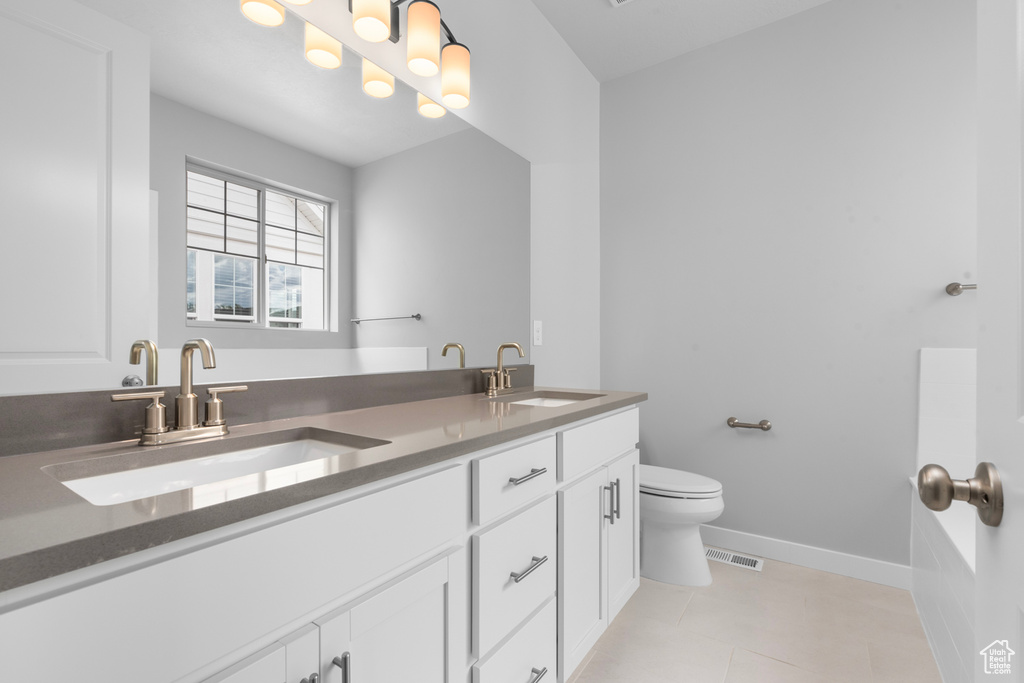 Bathroom featuring double vanity, toilet, tile patterned floors, and baseboards