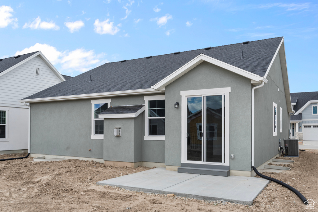 Back of property featuring cooling unit, roof with shingles, stucco siding, and a patio