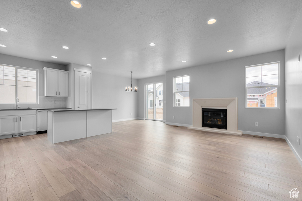 Kitchen with a sink, stainless steel dishwasher, a chandelier, recessed lighting, and a glass covered fireplace