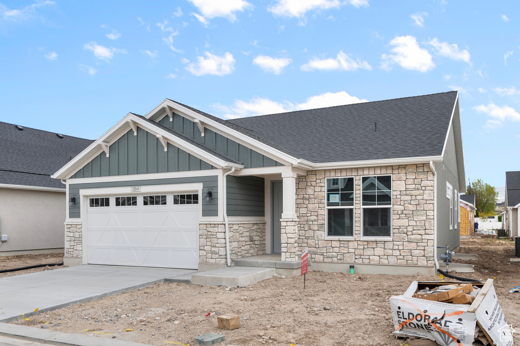 Craftsman inspired home with stone siding, board and batten siding, a garage, and driveway