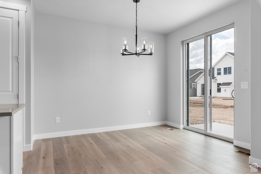 Unfurnished dining area featuring a chandelier, light wood finished floors, and baseboards