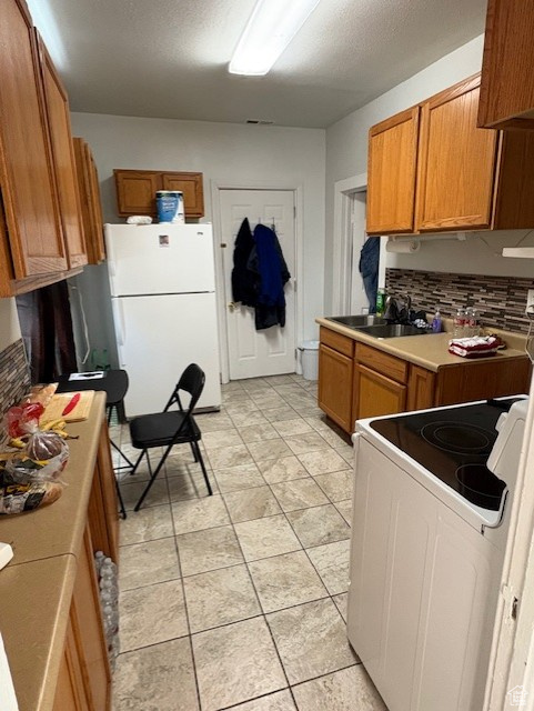 Kitchen with white appliances, a sink, brown cabinetry, backsplash, and light countertops