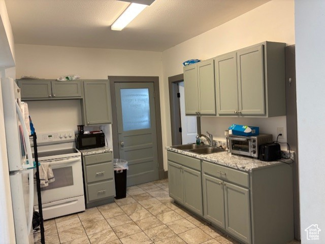 Kitchen featuring white appliances, a sink, light countertops, and gray cabinets