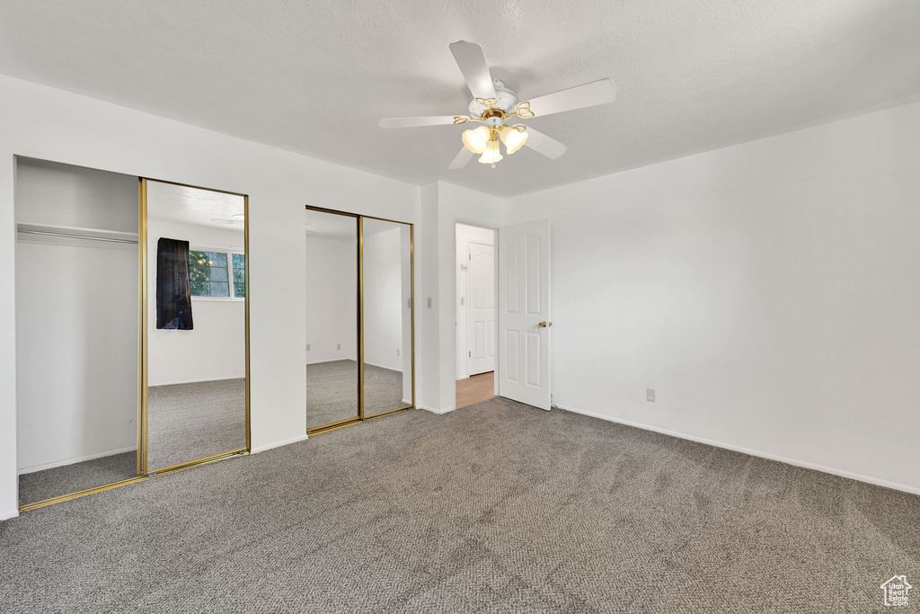 Unfurnished bedroom with two closets, carpet floors, baseboards, and ceiling fan