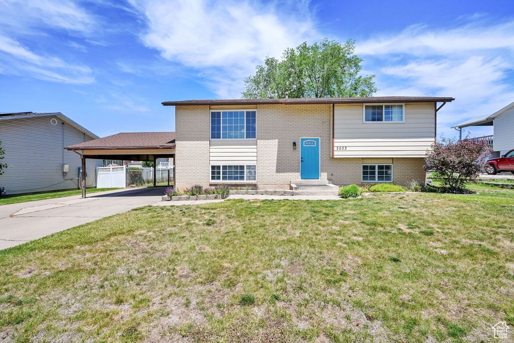 View of front of house featuring a carport, driveway, brick siding, and a gate