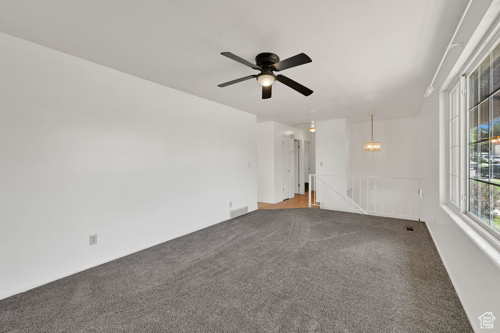 Carpeted empty room featuring a ceiling fan and a chandelier