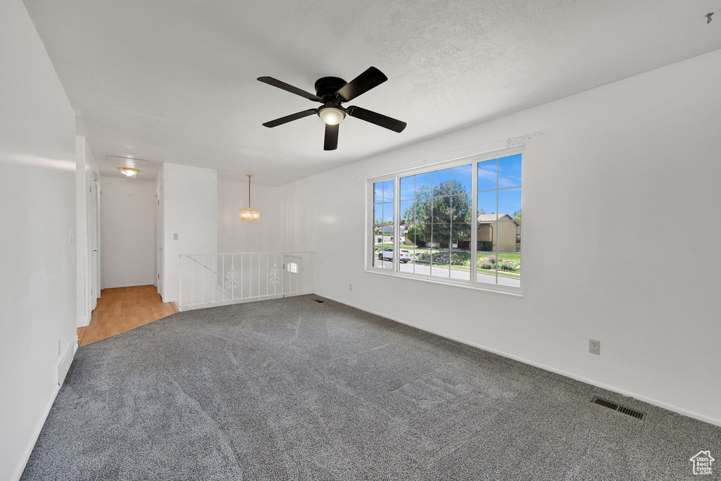 Carpeted spare room featuring ceiling fan, a chandelier, and baseboards
