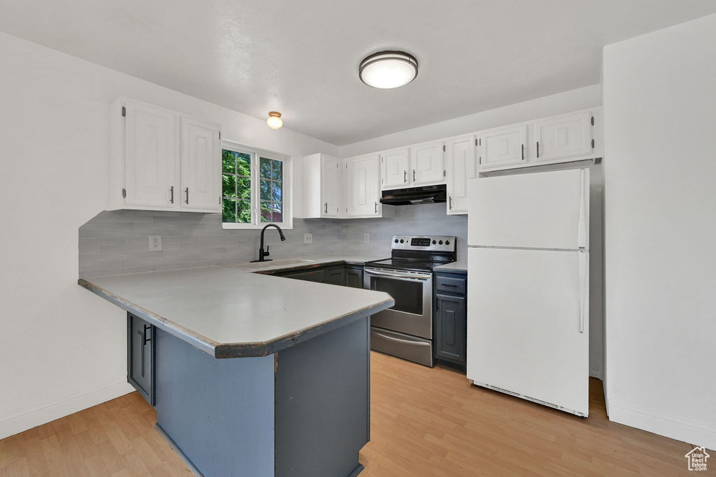 Kitchen featuring freestanding refrigerator, electric stove, under cabinet range hood, a sink, and white cabinetry