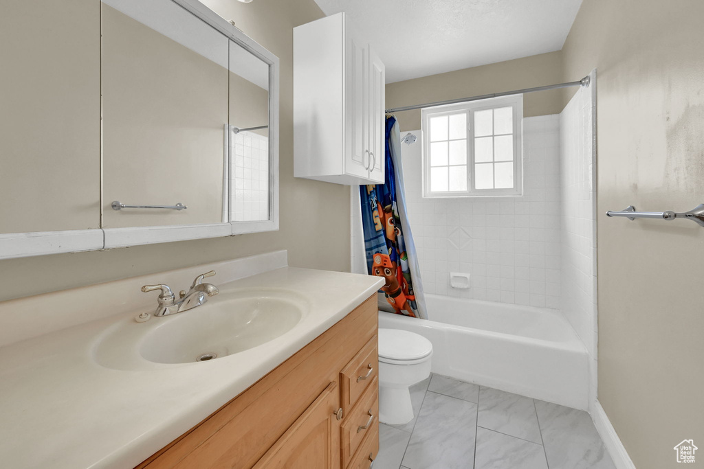 Bathroom with vanity, toilet, shower / tub combo, marble finish flooring, and baseboards
